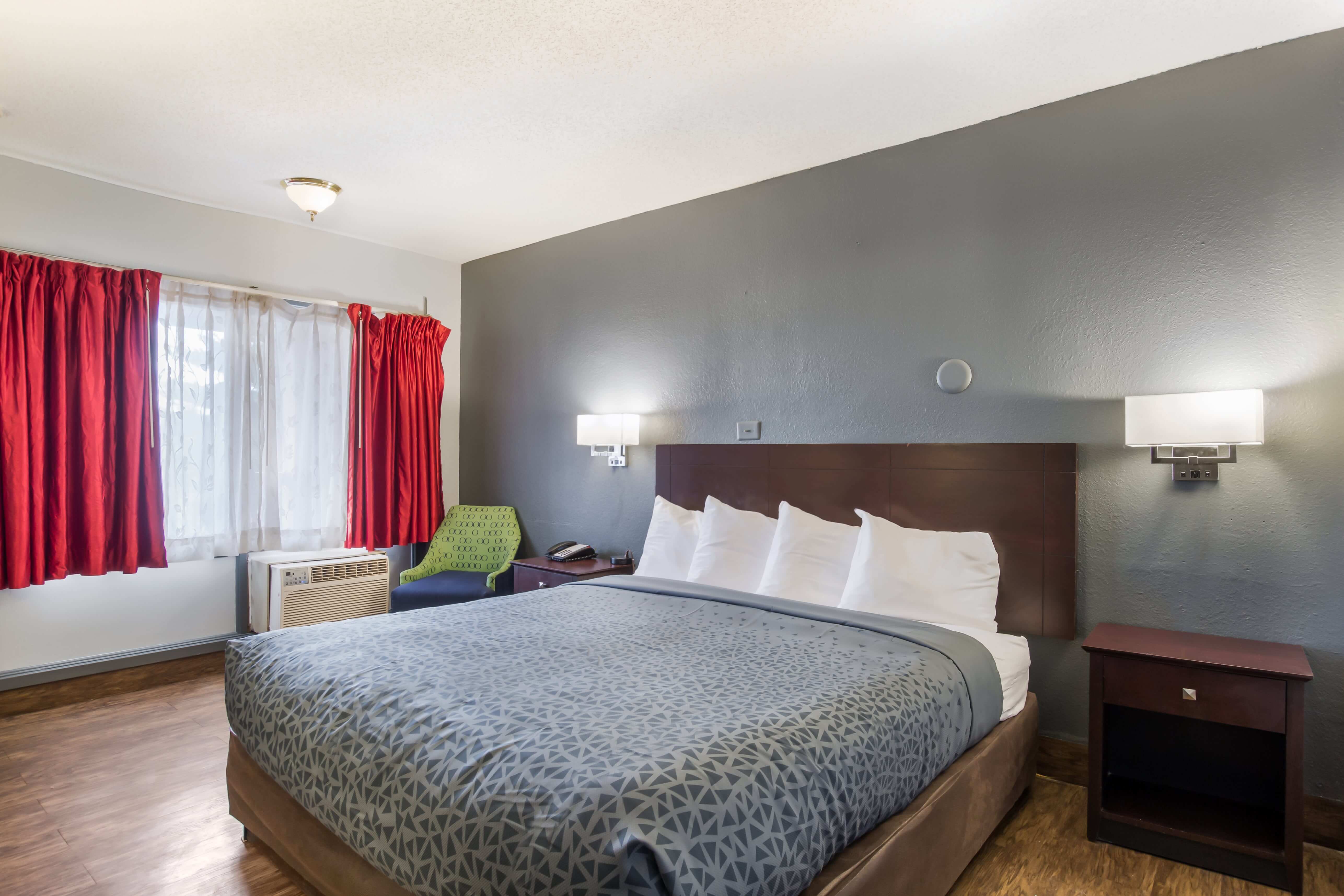 A wide view of a standard hotel room with a bed, nightstand, chair, and window.