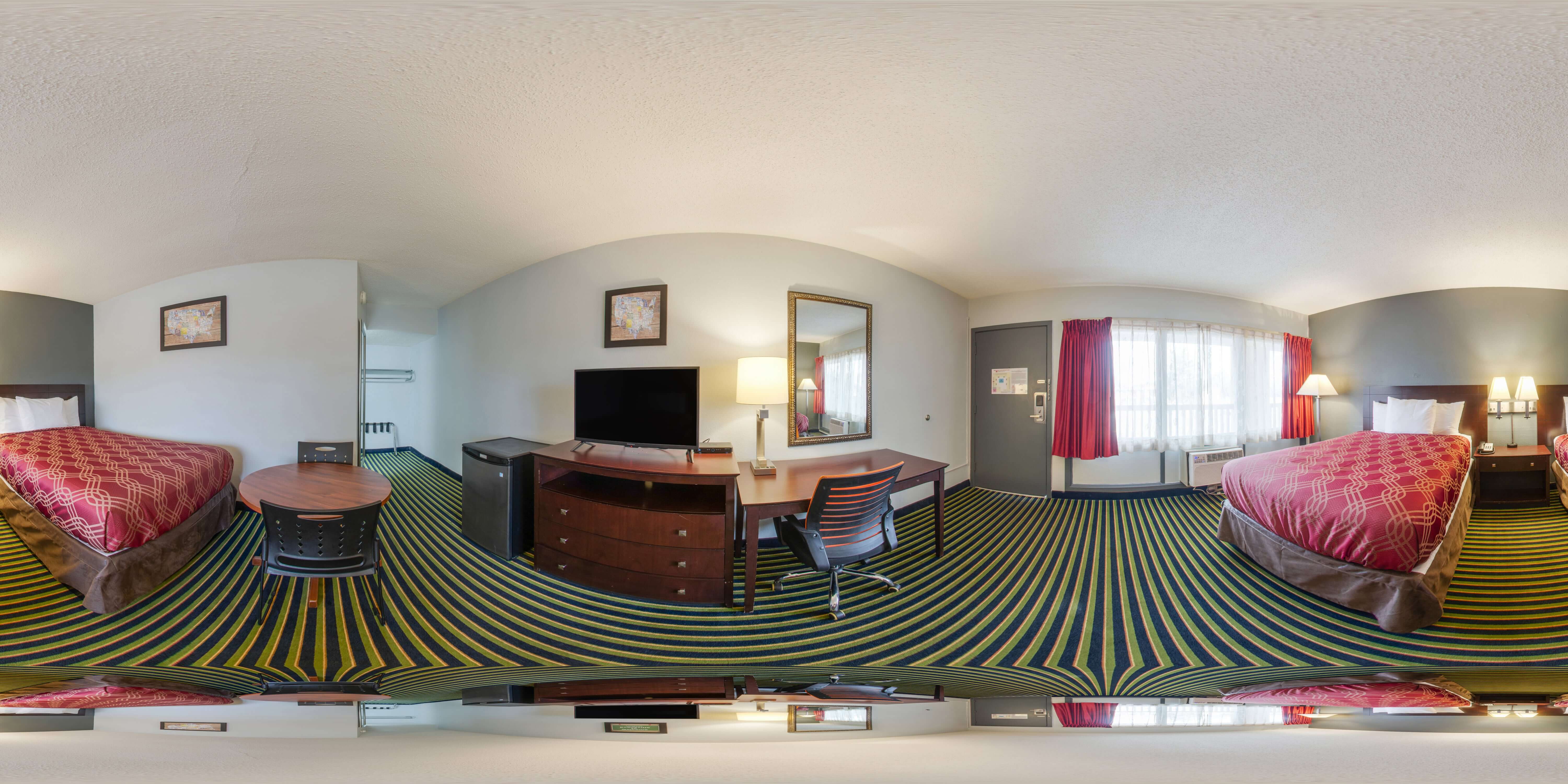 A wide-angle view of a hotel room with two beds, a desk, a TV, and a table.