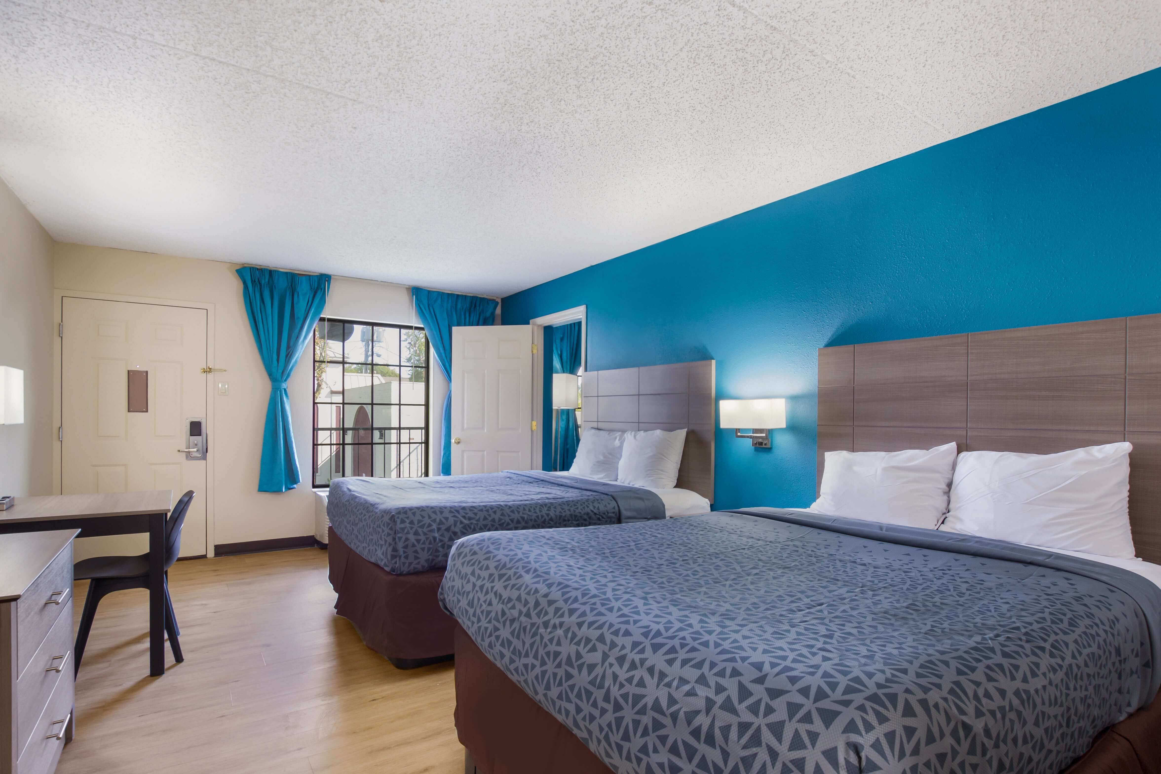 A hotel room with two beds, a desk, and a window.