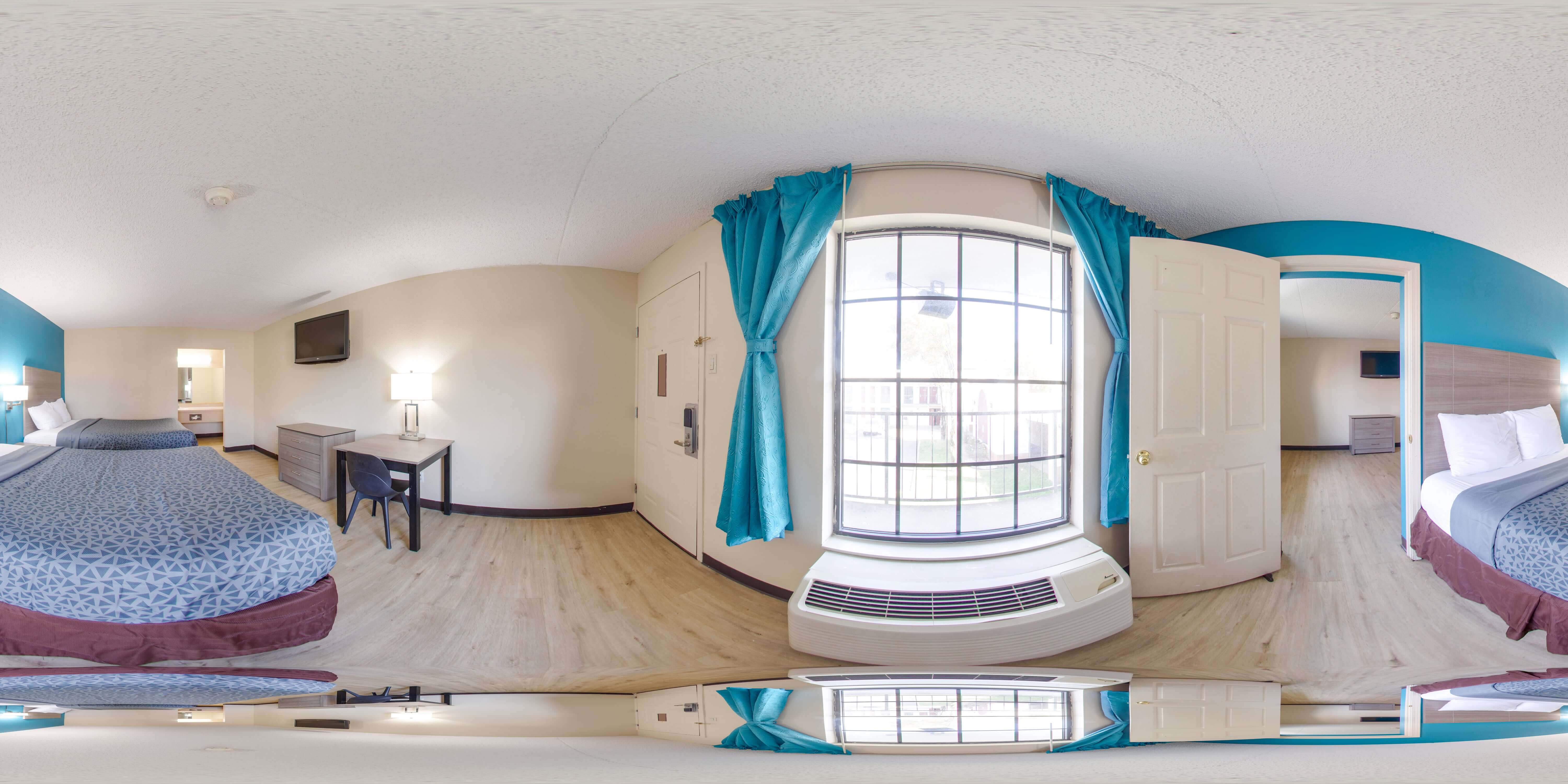 A wide-angle view of a hotel room with two beds, a desk, and a large window.