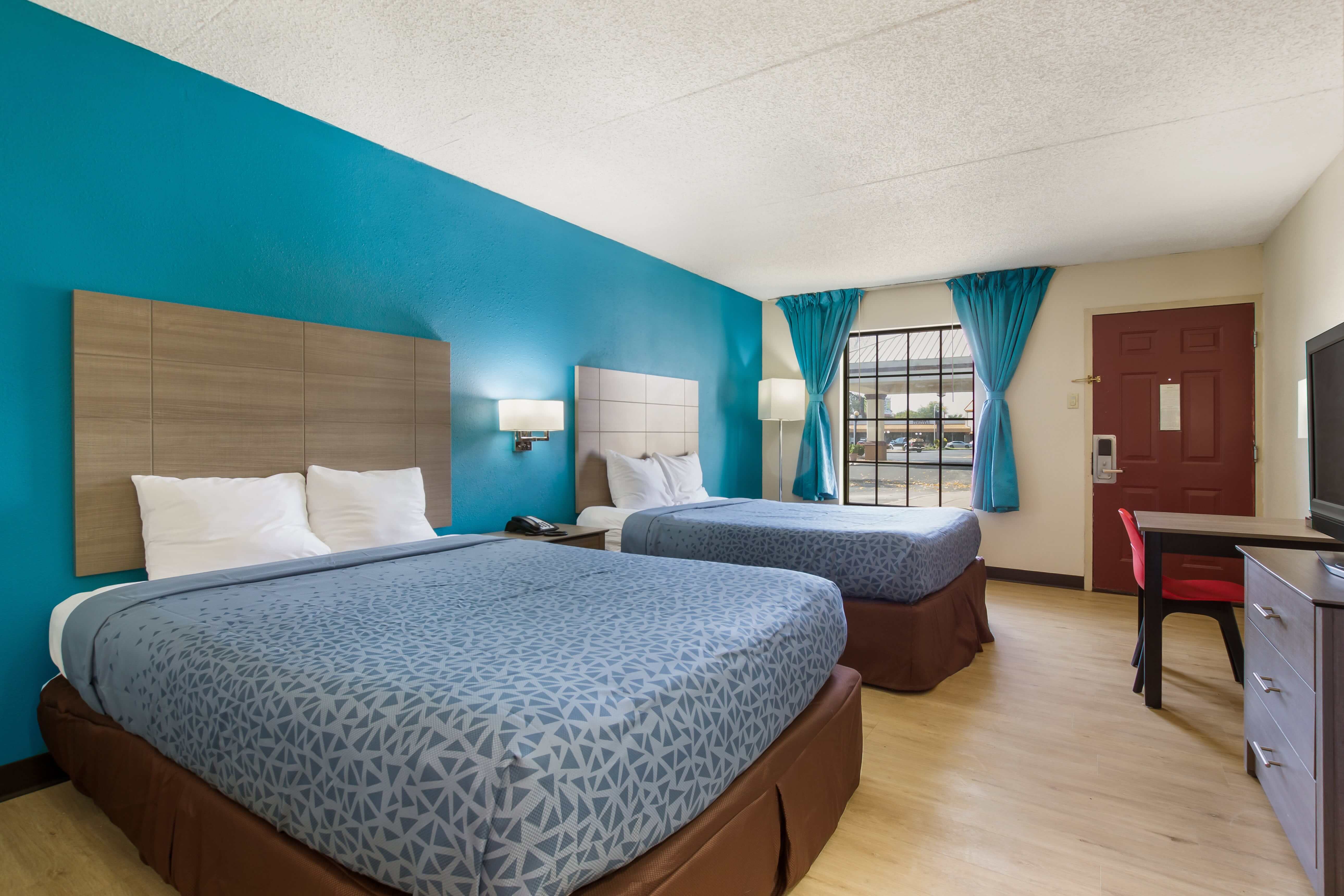 A hotel room with two beds, a desk, and a window.